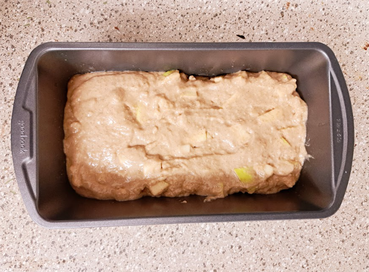 an overhead shot of apple spice loaf batter in a dark gray loaf pan